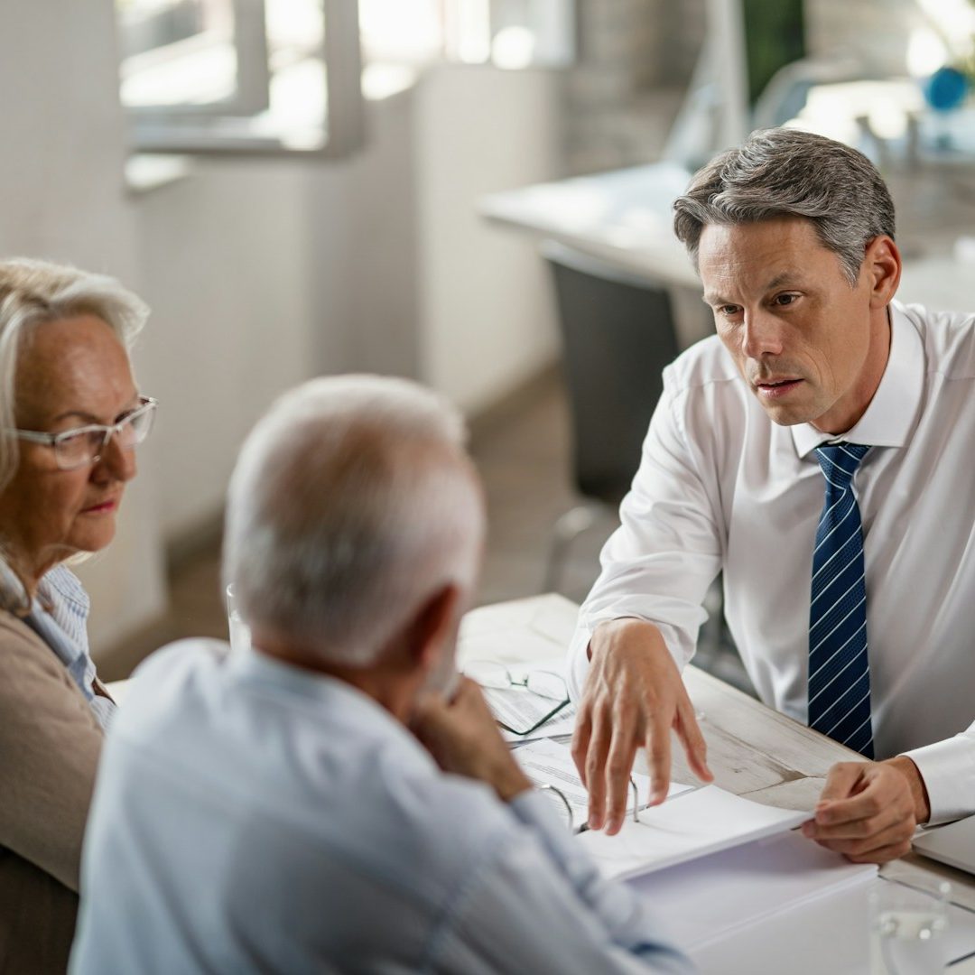 Consultation A lawyer discusses estate plans with an elderly couple in a bright office setting.