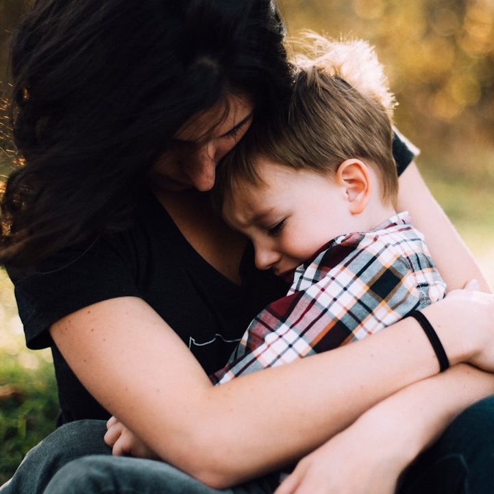 Family A woman holds a boy close, both sharing a tender moment outdoors.